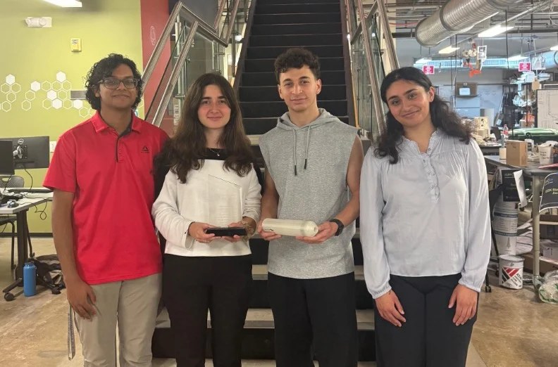 the four members of team retinex standing in the oshman engineering design kitchen holding the handheld prototype